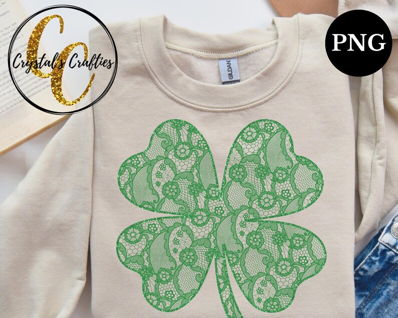 May include: A green four-leaf clover design with a lace pattern on a beige sweatshirt. The design is a digital graphic.