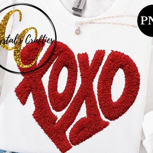 Puede incluir: Sudadera blanca con un gran dise&ntilde;o de coraz&oacute;n XOXO rojo. Las letras tienen una apariencia texturizada y difusa. Un logotipo dorado con purpurina de "Crystal's Crafties" est&aacute; en la esquina superior izquierda. Se ve un collar peque&ntilde;o con un colgante de flor.