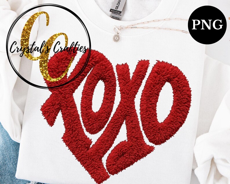 Puede incluir: Sudadera blanca con un gran dise&ntilde;o de coraz&oacute;n XOXO rojo. Las letras tienen una apariencia texturizada y difusa. Un logotipo dorado con purpurina de "Crystal's Crafties" est&aacute; en la esquina superior izquierda. Se ve un collar peque&ntilde;o con un colgante de flor.