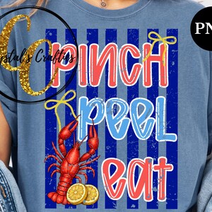 May include: Blue t-shirt with a graphic design featuring the words "Pinch Peel Eat" in red and blue, with a red crawfish and lemon slices. The design is set against a blue and white striped background.