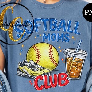 May include: Blue t-shirt with a softball-themed graphic. The design includes a yellow softball, cleats, a drink with ice, and the words "SOFTBALL MOMS CLUB" in blue and red. The shirt has a relaxed fit.