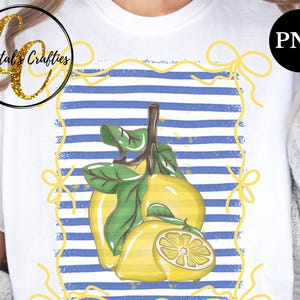 May include: A white t-shirt with a blue and white striped design and a graphic of lemons. The lemons are yellow and green and have a rustic, vintage look. The graphic is framed with a yellow rope design with bows at the corners.