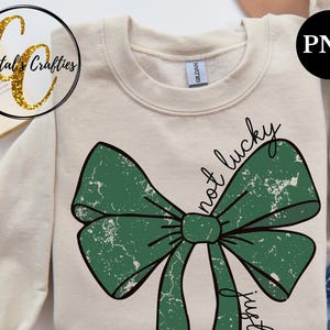May include: A beige sweatshirt with a green bow and the text "not lucky just gifted" in black.