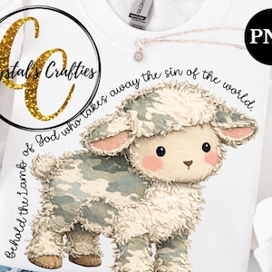 Op de afbeelding: Witte sweatshirt met een illustratie van een lam in camouflagepatroon. Het ontwerp bevat de tekst "Zie het Lam van God, dat de zonde der wereld wegneemt." Een goudglitter logo voor "Crystal's Crafties" is ook zichtbaar.