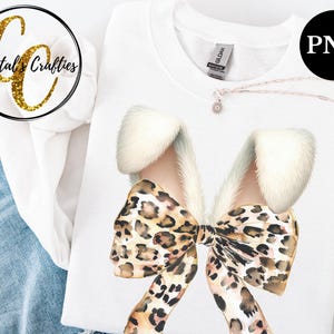 May include: A white t-shirt with a large leopard print bow with white fur accents. The bow is centered on the shirt.