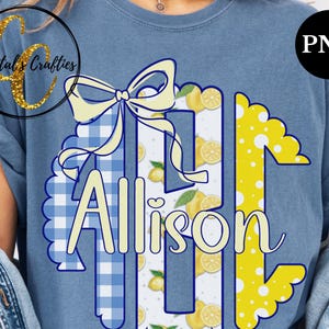 以下が含まれることがあります： 黄色、白、青のモノグラムデザインの青いTシャツ。モノグラムはレモンと水玉模様の弓の形をしています。「アリソン」という名前が黄色の文字で書かれています。