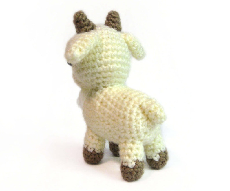 May include: A crocheted goat toy with brown horns and hooves. The goat is white and has a fluffy texture.