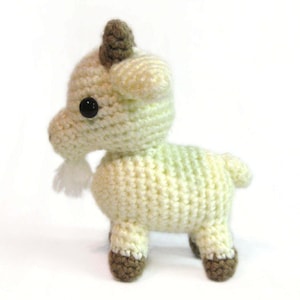 May include: A crocheted goat toy with a white and green body, brown hooves, and black eyes. The goat has a small white beard.