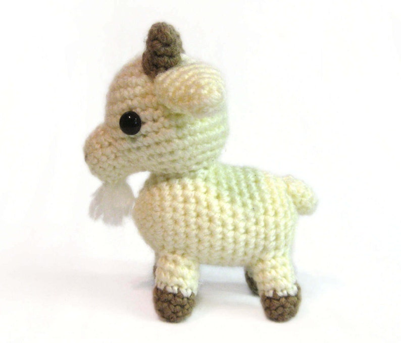 May include: A crocheted goat toy with a white and green body, brown hooves, and black eyes. The goat has a small white beard.