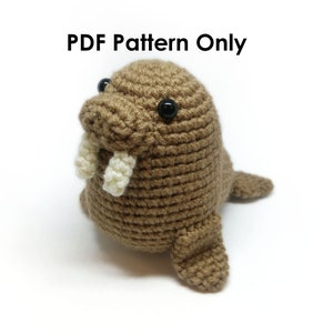 May include: A crocheted brown walrus with black eyes and white tusks. The handmade plush toy has flippers and is sitting upright. The text "PDF Pattern Only" is at the top of the image.