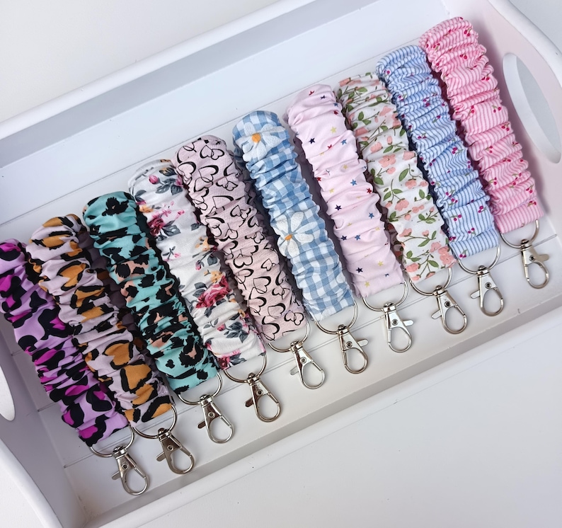 Pode incluir: Uma cole&ccedil;&atilde;o de chaveiros de pulso de tecido em v&aacute;rios padr&otilde;es e cores, incluindo estampa de leopardo, floral e xadrez. Cada chaveiro tem um fecho prateado para prender as chaves.