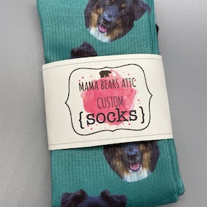 May include: A pair of teal blue socks with a custom design featuring a dog's face. The socks are packaged with a white label that reads "Mama Bears Attic Custom {socks}".