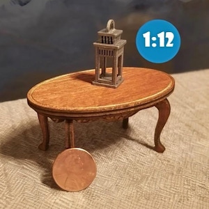 May include: A miniature wooden table with a decorative design on the top and three legs. A silver metal lantern sits on the table. The table is 1:12 scale.