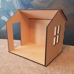 May include: A small, unfinished wooden house with a single window and a doorway. The house is made of brown cardboard and has a simple design.