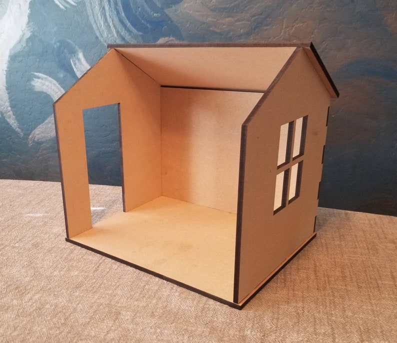May include: A small, unfinished wooden house with a single window and a doorway. The house is made of brown cardboard and has a simple design.
