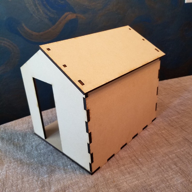May include: A small, unfinished wooden house model with a simple design. The house is made of plywood and has a flat roof. The house is about 6 inches tall and 4 inches wide.