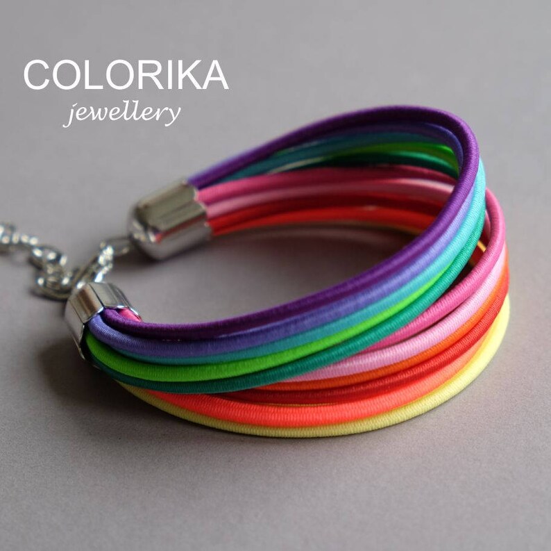 May include: A colourful rainbow bracelet made of multiple strands of elastic cord. The bracelet is secured with a silver clasp.