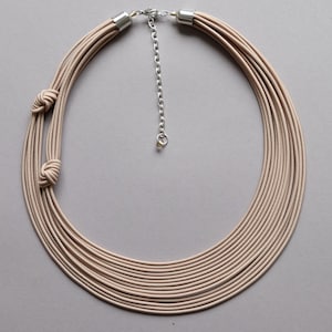 May include: A multi-strand necklace made of beige fabric with two knots. The necklace has a silver chain extender.
