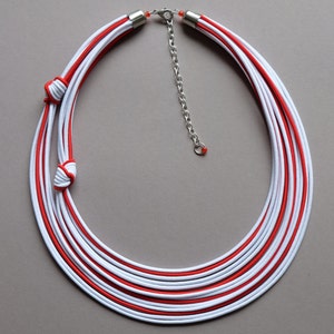 May include: A multi-strand necklace made of red and white cord, with a silver chain and clasp. The cord is knotted at the ends to create a layered effect.