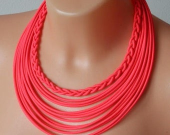 May include: A bright pink multi-strand necklace made of braided cord. The necklace is layered and has a chunky, bold look.