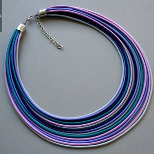 Può includere: Una collana multifilo realizzata con cordoncini sottili e colorati in tonalità di viola, rosa, turchese e bianco. La collana ha una chiusura argentata.