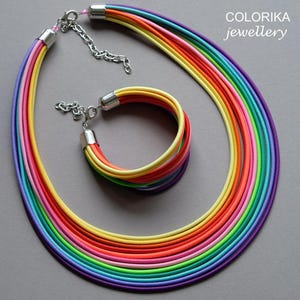 May include: A multi-strand necklace and bracelet set in rainbow colours. The necklace and bracelet are made from multiple strands of colourful fabric.