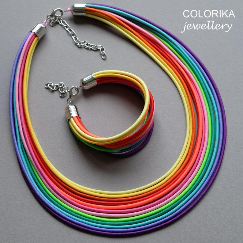 May include: A multi-strand necklace and bracelet set in rainbow colours. The necklace and bracelet are made from multiple strands of colourful fabric.