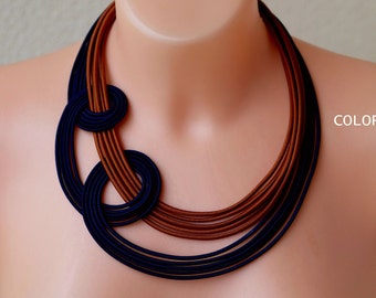 May include: A multi-layered necklace made of brown and navy blue fabric. The necklace is arranged in a circular pattern with a knot at the center.