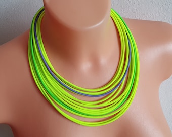 May include: A layered necklace featuring multiple strands of neon yellow, green, and purple cords. The necklace is displayed on a mannequin, showcasing its vibrant colors and modern design. This statement piece is a bold accessory.