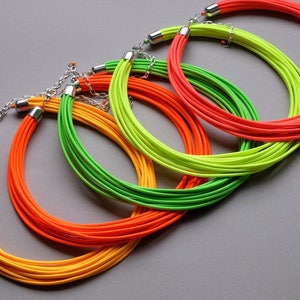 May include: Four colorful necklaces made of layered cords in yellow, orange, green, and red. The necklaces are connected by silver clasps.