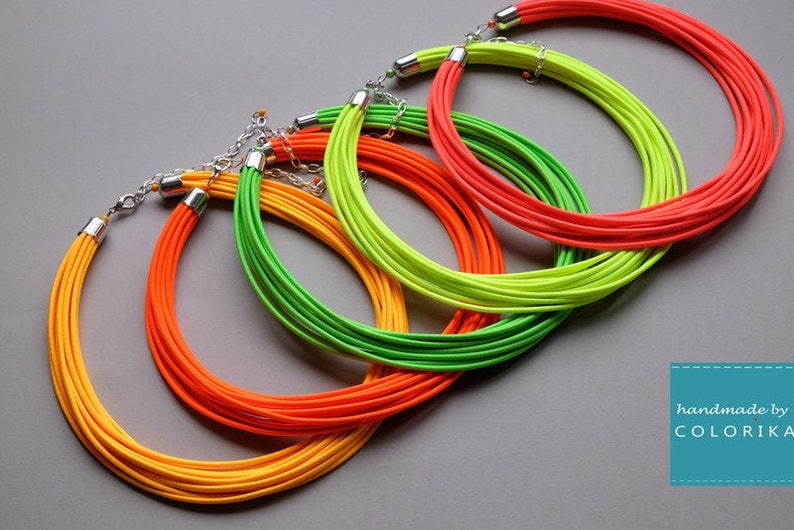 May include: Four colorful necklaces made of layered cords in yellow, orange, green, and red. The necklaces are connected by silver clasps.