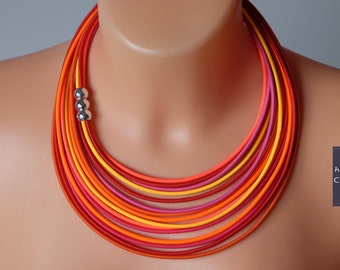 May include: A multi-layered necklace made of red, orange, and yellow fabric cords. The necklace has a silver bead accent.