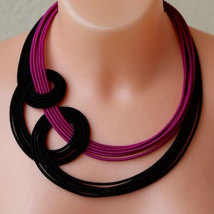 Può includere: Una collana multistrato con uno schema di colori nero e magenta. La collana è realizzata in tessuto e ha un design annodato.