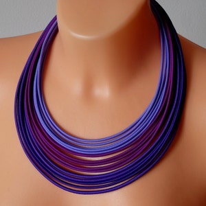 May include: A multi-layered necklace made of purple and lavender fabric. The necklace is made of many thin strips of fabric that are layered on top of each other to create a gradient effect.