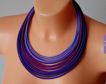 May include: A multi-layered necklace made of purple and lavender fabric. The necklace is made of many thin strips of fabric that are layered on top of each other to create a gradient effect.