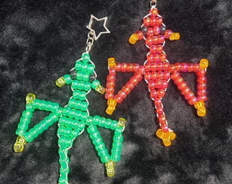 May include: Two beaded dragon-shaped keychains, one in green and one in red, each featuring a silver-toned star-shaped clasp. The green dragon has yellow accents, while the red dragon has orange accents, both constructed from small, translucent plastic beads.