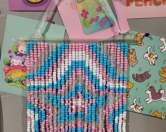 Puede incluir: Un tapiz de pared hecho de hilos verticales de cuentas de plástico en rosa, blanco y azul claro, dispuestas para formar un patrón de estrella. Las cuentas están ensartadas en una varilla de plástico transparente con una cinta blanca.