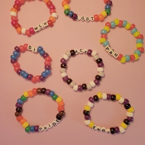 May include: Seven colorful beaded bracelets with different letters spelling out "LGBT", "WLLW", "BI", "ACE", "PAN", "PRIDE", and "ENBY".