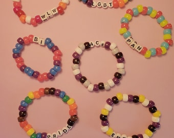 May include: Seven colorful beaded bracelets with different letters spelling out "LGBT", "WLLW", "BI", "ACE", "PAN", "PRIDE", and "ENBY".