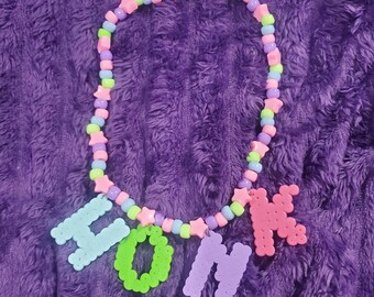 May include: A beaded necklace featuring a circular strand of alternating light blue, lime green, and lavender round beads interspersed with small pink star-shaped beads. Four large, textured letter-shaped charms spell out the word HONK.