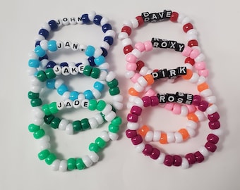 May include: A stack of eight colorful beaded bracelets with different names spelled out in black beads. The names are John, Jane, Jake, Jade, Dave, Roxy, Dirk, and Rose.