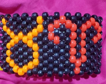 May include: A black, orange, and red beaded bracelet with a repeating pattern. The bracelet is made of small, round beads.