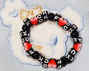 May include: Black beaded bracelet with white letters spelling "FCK" and red heart charms.