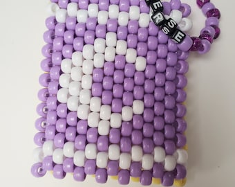 May include: A purple and white beaded keychain with a purple beaded bracelet attached. The bracelet has the word "DESSERT" spelled out in black beads.