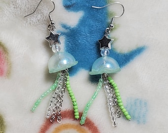 May include: A pair of silver dangle earrings with a light blue iridescent jellyfish charm and green and clear bead accents.
