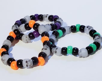May include: Three colorful bracelets made with black, white, orange, purple, and green skull beads.