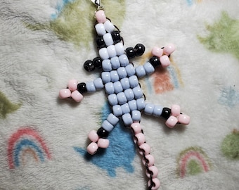 May include: A beaded lizard keychain with a light blue body, pink legs, and a black tail. The keychain has a silver clasp.