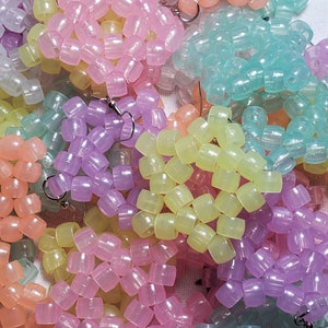 May include: A close-up of a collection of pastel-colored beaded earrings. The earrings are made of small, round beads that are strung together in a variety of patterns. The beads are translucent and have a slight shimmer to them. The earrings are all different colors, including pink, purple, yellow, and blue.