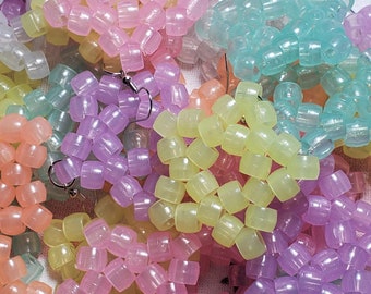 May include: A close-up of a collection of pastel-colored beaded earrings. The earrings are made of small, round beads that are strung together in a variety of patterns. The beads are translucent and have a slight shimmer to them. The earrings are all different colors, including pink, purple, yellow, and blue.