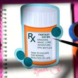 The image shows a sticker shaped like an orange and white medical pill bottle. The bottle is for the fantasy genre in books, movies, television, and other forms of media. The design is accented with teal. The pills with swords and a dragon silhouette  on it. The text reads- Fantasy D20mg. 
Dragons, magic lore, adventure, epic battles. 
Take to escape the boring realities of life.